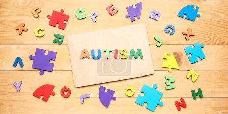 Photo for Word AUTISM, letters and puzzle pieces on wooden background - Royalty Free Image