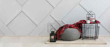 Photo for Table with cup, books, plaid, knitted pouf and lantern near grey wall in room. Banner for design - Royalty Free Image