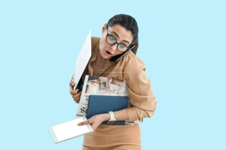 Téléchargez les photos : Jeune femme d'affaires choquée avec montre-bracelet, appareils et journaux sur fond bleu - en image libre de droit