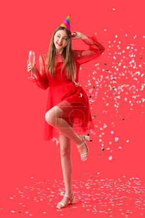 Happy young woman with glass of champagne celebrating Birthday on red background