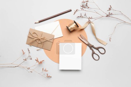 Komposition mit Blanko-Karte, Umschlägen, Schere, Band und getrockneten Blumen auf weißem Hintergrund