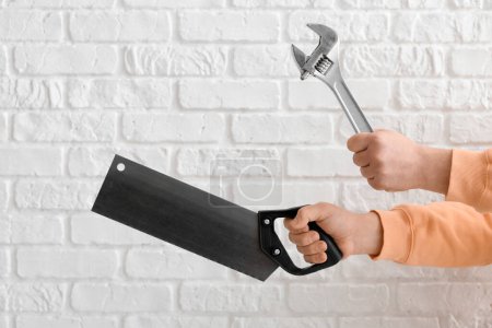 Téléchargez les photos : Travailleur avec clé et scie à main sur fond de brique blanche - en image libre de droit