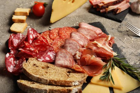 Photo for Slate plate with assortment of tasty deli meats, bread and cheese on grey background - Royalty Free Image