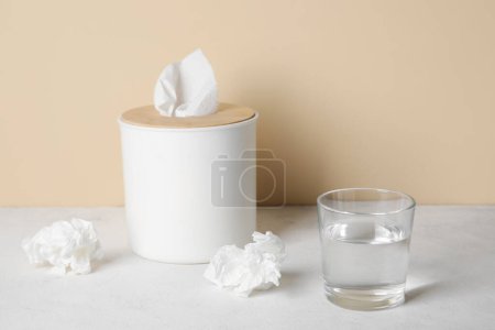 Photo for Glass of water with tissue box on table near beige wall. Allergy concept - Royalty Free Image