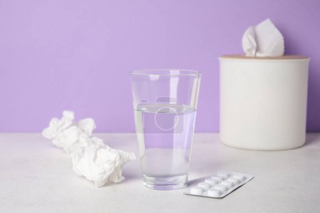 Photo for Glass of water with pills and tissue box on table near lilac wall. Allergy concept - Royalty Free Image