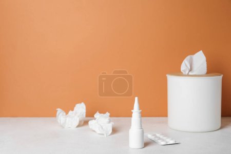 Foto de Gotas nasales con pastillas y caja de tejido en la mesa cerca de la pared naranja. Concepto de alergia - Imagen libre de derechos