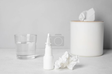 Photo for Nasal drops with tissue box and glass of water on table near grey wall. Allergy concept - Royalty Free Image