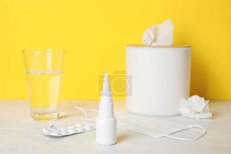 Photo for Nasal drops with pills, medical mask. glass of water and tissue box on table near yellow wall. Allergy concept - Royalty Free Image