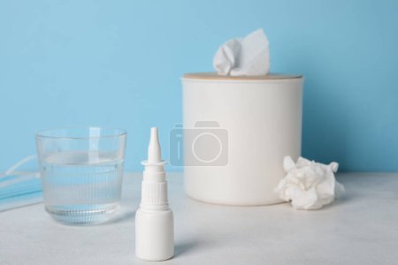 Photo for Nasal drops with glass of water and tissue box on table near blue wall. Allergy concept - Royalty Free Image