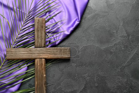 Holzkreuz mit Palmblatt und violettem Stoff auf dunklem Hintergrund. Karfreitagskonzept