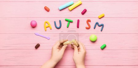 Photo for Child's hands with plasticine and word AUTISM on pink wooden background - Royalty Free Image