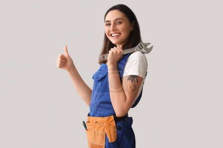 Photo for Female plumber with wrench showing thumb-up on grey background - Royalty Free Image