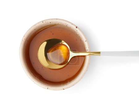 Bowl and spoon of tasty maple syrup on white background