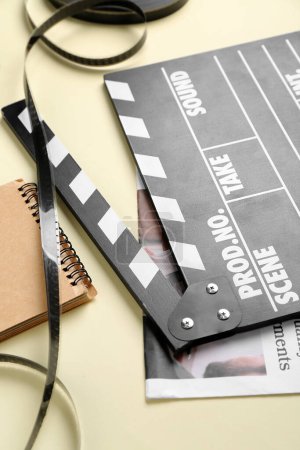 Photo for Movie clapper with newspaper, notebook and film on beige background, closeup - Royalty Free Image