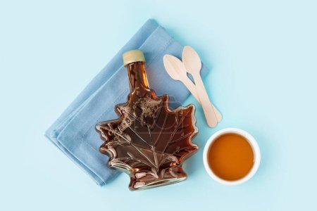 Photo for Bottle with saucer of tasty maple syrup on blue background - Royalty Free Image