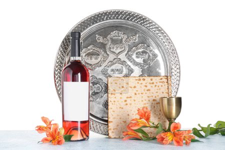 Passover Seder plate, bottle of wine, cup, flatbread matza and alstroemeria flowers on table against white background