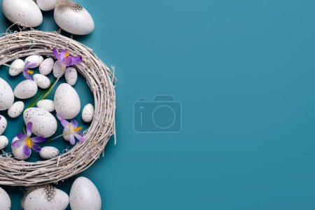 Wreath with Easter eggs and beautiful crocus flowers on blue background