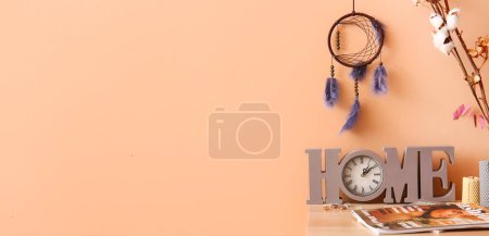 Stylish dream catcher hanging on beige wall and table with clock and fashion magazines. Banner for design
