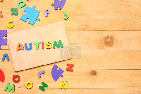 Photo for Word AUTISM with letters and puzzle pieces on wooden background - Royalty Free Image