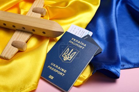 Passport with toy airplane and flag of Ukraine on pink background, closeup