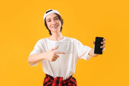 Téléchargez les photos : Cool adolescent garçon pointant vers le téléphone mobile sur fond jaune - en image libre de droit