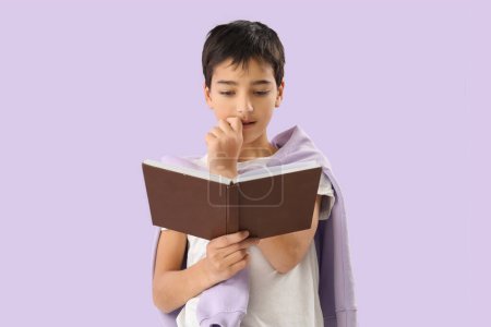 Téléchargez les photos : Petit garçon avec livre mordant ongles sur fond lilas - en image libre de droit