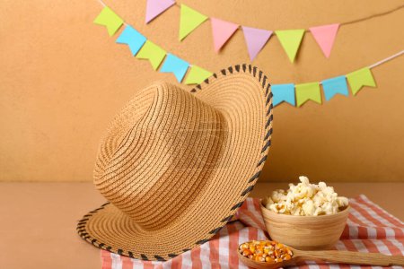 Foto de Cuenco de palomitas de maíz con cuchara y sombrero de paja sobre mesa beige. Festa Junina (Festival de Junio) celebración - Imagen libre de derechos