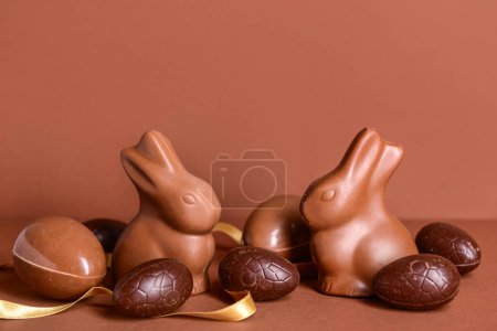 Photo for Chocolate Easter eggs, bunnies and ribbon on brown background - Royalty Free Image