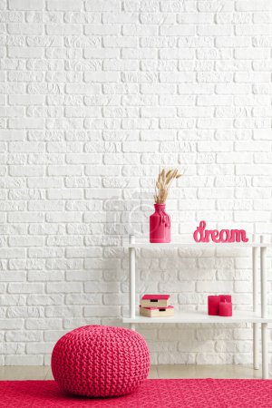 Photo for Viva magenta pouf and table with decor near white brick wall in room - Royalty Free Image