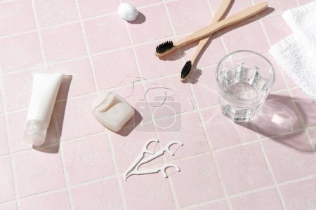 Foto de Hilo dental, mondadientes, cepillos, pasta de dientes y vaso de agua sobre tabla de baldosas rosadas - Imagen libre de derechos