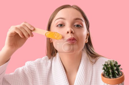 Photo for Young woman holding spatula with sugaring paste and cactus on pink background - Royalty Free Image