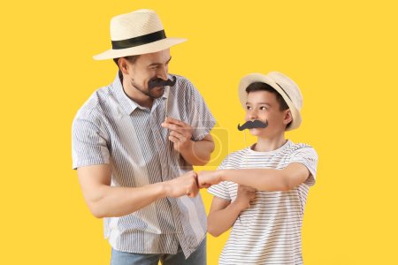 Porträt des Vaters und seines kleinen Sohnes mit Papierschnurrbart, der die Fäuste auf gelbem Hintergrund schlägt