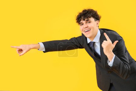 Photo for Laughing young businessman showing loser gesture and pointing at something on yellow background - Royalty Free Image
