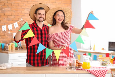 Junges Paar mit Fahnen feiert Festa Junina (Juni-Fest) in der Küche