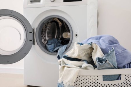 Téléchargez les photos : Panier à linge avec vêtements sales et machine à laver près du mur de lumière dans la chambre - en image libre de droit