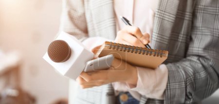 Photo for Female journalist with microphone, notebook and phone in office, closeup - Royalty Free Image