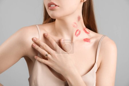 Foto de Mujer joven con mordedura de amor y marcas de lápiz labial en el cuello contra fondo gris, primer plano - Imagen libre de derechos
