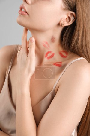 Foto de Mujer joven con mordedura de amor y marcas de lápiz labial en el cuello contra fondo gris, primer plano - Imagen libre de derechos