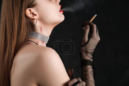 Foto de Hermosa joven con mordeduras de amor en su cuello fumar cigarrillo contra el fondo oscuro, primer plano - Imagen libre de derechos