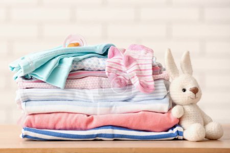 Téléchargez les photos : Empilement de vêtements de bébé, sucette et jouet sur la table, gros plan - en image libre de droit