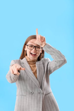 Photo for Young businesswoman showing loser gesture and pointing at viewer on blue background - Royalty Free Image