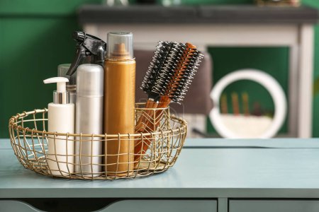 Basket with different hair sprays and brushes on table in beauty salon