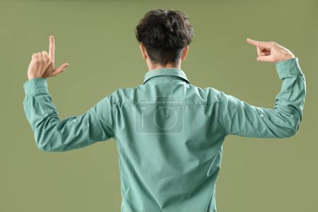 Photo for Young man showing loser gesture on green background, back view - Royalty Free Image