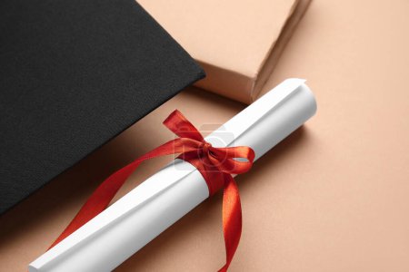 Photo for Diploma with red ribbon, graduation hat and book on brown background - Royalty Free Image