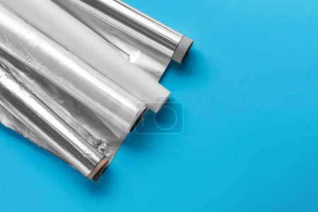 Rolls of aluminium foil, food film and baking paper on color background