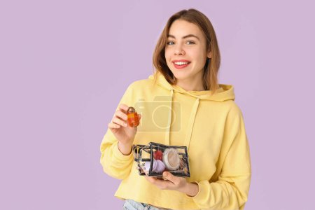 Téléchargez les photos : Jeune femme avec sac cosmétique transparent sur fond lilas - en image libre de droit