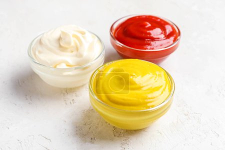 Schalen mit Ketchup, Mayonnaise und Senf auf weißem Grunge-Tisch