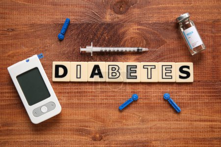 Word DIABETES with glucometer, syringe and insulin on wooden background