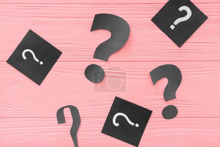 Paper question marks on pink wooden background