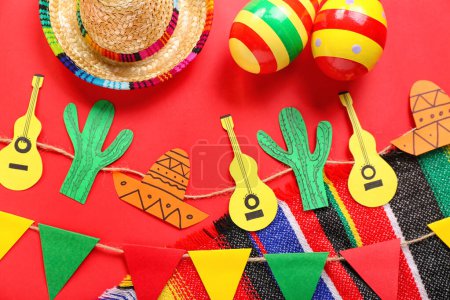 Mexikanische Maracas mit Sombrero-Hut, Papiergirlande und Fahnen auf rotem Hintergrund